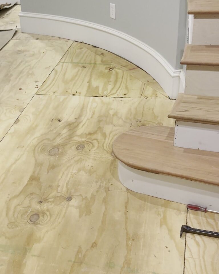 Plywood subfloor installed over a concrete slab in a foyer next to a staircase