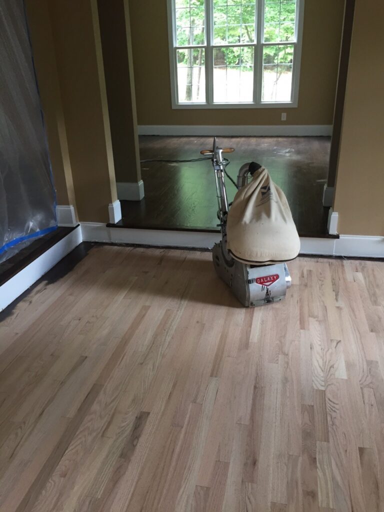 Oak floor mid-refinish: bare sanded wood in front, old dark finish in the back